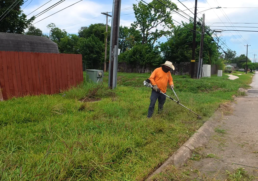 aiken lawn service trimming — crew member string trimming overgrown grass along fence line